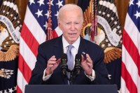 A photo of President Biden speaking at a podium in front of American flags.