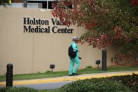 An unidentifiable person in scrubs walks beside a tan wall with a sign reading "Holston Valley Medical Center" on it.
